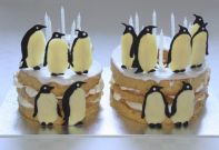Penguin Cake - Layers of moist almond cake (gluten free) sandwiched together with lashings of whipped cream and lemon sauce, coated with lemon glace icing and decorated with hand made chocolate penguins.
